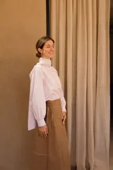 Camisa de algodón a rayas verticales rosas y blancas, con cuello alto y lazo grande en el cuello.