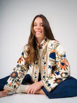 Chaqueta corta color crema con bordados de flores en tonos naranja, azul y verde.