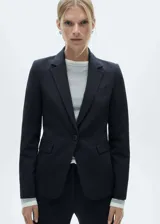 Blazer entallado color negro con cuello de pico con solapa y muesca, manga larga con puños abotonados, dos bolsillos de ribete en la parte delantera, un bolsillo de ribete en el pecho, cierre de botones en la parte delantera, abertura posterior en el bajo y forro interior.