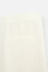 Pantalón color crema de lino, corte amplio, con pliegues frontales, bolsillos laterales y traseros de ojal. Cierre frontal con cremallera y gancho metálico oculto.