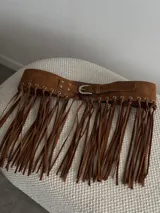 Cinturón ancho de gamuza color marrón con hebilla metálica plateada y flecos largos.