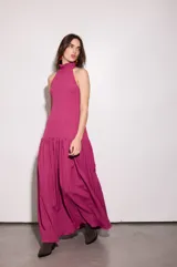 Vestido largo fucsia con escote halter y espalda baja. Tiene volado en el cuello y maxi volado en la cadera.
