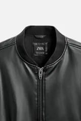 Cazadora bomber negra de efecto piel, corte relaxed fit, con cuello y puños de rib elástico, cierre frontal con cremallera, bolsillos laterales de doble vivo y bolsillo interior.