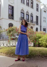 Vestido midi a rayas verticales azules y blancas, con cuerpo superior fruncido y falda amplia. Presenta un detalle de flor roja en el hombro.