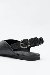 Zapato destalonado de punta fina, color negro, con base baja y tira trasera elástica con hebilla metálica ajustable. Diseño minimalista.