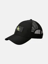 Gorra tipo trucker negra con visera curva. Presenta un panel frontal de sarga y paneles traseros de malla. En el frente lleva un parche rectangular negro con el logo de Calvin Klein en color amarillo neón.
