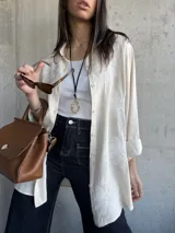Camisa beige con bordados florales blancos, de corte recto y mangas largas con puños enrollados.