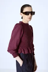 Blusa color borgoña con escote redondo con volados, mangas largas abullonadas y cuerpo fruncido.