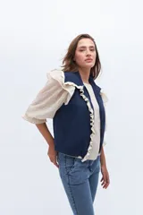 Chaleco de punto sin mangas, color azul marino, con cuello y frente adornados con volados en contraste de color blanco o crudo.