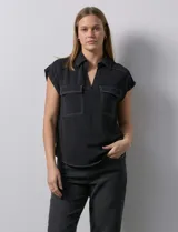 Blusa negra Ninety con cuello con solapa y escote en V. Tiene dos bolsillos frontales y pespuntes blancos en contraste.