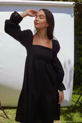 Vestido de lino negro con escote recto, mangas largas abullonadas y detalles elásticos.