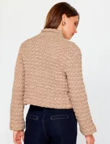 Campera corta de mujer color beige, con textura capitoneada irregular y cuello alto abotonado. Presenta cierre frontal oculto y bolsillos laterales.