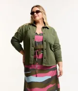 Campera plus size color verde militar, modelo oversized, confeccionada en sarga texturizada. Cuenta con cuello tradicional, cierre abotonado, dos bolsillos delanteros y puños abotonados.