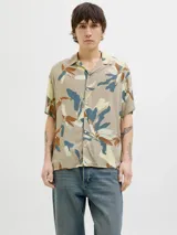 Camisa de manga corta con estampado de hojas en tonos beige, azul y marrón. Tiene cuello resort, cierre con botones y corte relajado.