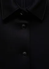 Chaqueta corta negra con cuello camisero, cierre frontal con botones, dos bolsillos laterales y forro interior.