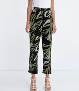 Pantalón pijama fluido de viscosa con estampado de hojas en tonos verde y gris sobre fondo negro. Tiene cintura media con ajuste de cordón con punteras metálicas, bolsillos laterales y pinzas frontales.