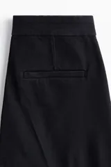 Jean de denim negro con leve stretch, corte ajustado de cintura a cadera y acampanado desde la rodilla al bajo. Es de tiro alto con cierre, botón oculto y corchete. Tiene bolsillos traseros decorativos y pliegues delanteros y traseros.