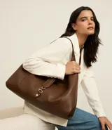 Cartera tipo hobo grande de color marrón oscuro, confeccionada en PU (poliuretano) con textura que imita cuero granulado. Presenta un asa de mano y un detalle de tira con hebilla metálica en la parte frontal superior.