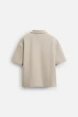 Polo color beige de corte relaxed fit, confeccionado en tejido interlock de algodón con elasticidad. Tiene cuello solapa y cierre frontal de cremallera.
