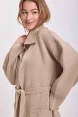 Cardigan largo de punto color beige con cuello solapa, bolsillos laterales y lazo para ajustar en la cintura.