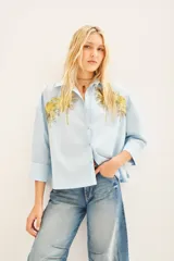 Camisa celeste de poplin con bordados de palmeras doradas en el frente, de corte amplio, con cuello y cartera.