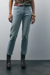 Pantalón de jean gris oscuro, de corte mom fit, tiro alto y largo tobillero. Cuenta con cinco bolsillos, cierre frontal con cremallera y botón.