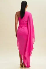 Vestido largo de fiesta fucsia, con un solo hombro y manga larga tipo capa. Tiene un corte ajustado con drapeado en la cintura y abertura lateral en la falda.