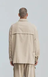 Camisa beige de manga larga, estilo técnico con múltiples bolsillos delanteros y un bolsillo en la parte inferior de la espalda, botones en la cartera y mangas, calce oversize, confeccionada en textil ligero suave al tacto.