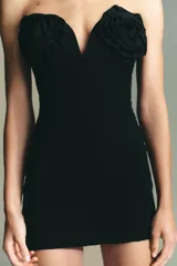 Vestido corto negro con escote corazón rígido y hombros descubiertos. Presenta detalle de flores en relieve en el pecho y cierre trasero con cremallera oculta.