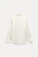 Camisa negra de satén con cuello solapa, manga larga, bolsillos con solapa en el delantero, bajo asimétrico y cierre frontal con botones.