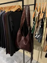 Bolso de 100% cuero color marrón, con correa regulable y detalles en tachas, perfecto para transportar una computadora.