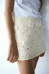 Minifalda entallada de tiro bajo, confeccionada en tejido bordado color crudo con apliques florales. Posee pinzas en la parte trasera y cierre oculto en un lateral.