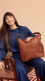 Cartera tipo hobo de cuero sintético color marrón con correa corta y correa larga ajustable. Tiene un bolsillo con cierre en el frente y otro en la parte trasera, además de bolsillos internos.