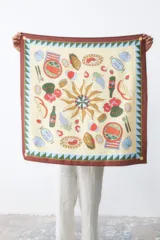 Pañuelo cuadrado de seda color crema con estampado de motivos gastronómicos y borde marrón con diseño geométrico.