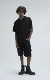 Camisa negra de tejido de punto calado con diseño de zigzag, cuello polo, manga corta y cierre frontal con botones.