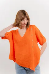 Blusa blanca de lino con escote en V, mangas cortas con vuelta y botones decorativos en el hombro.