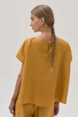 Blusa color mostaza confeccionada en lino, con cuello bote y mangas cortas.