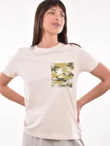 Remera color crudo de corte recto, con cuello redondo y bolsillo en el pecho con estampado camuflado en tonos verdes y marrones.