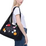 Bolso tipo shopper de malla negra con diseño de flores de crochet de colores. Tiene cierre con tiras de cuero y una bolsa interior extraíble con cremallera.