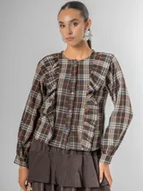 Camisa de tela escocesa liviana, color gris oscuro con líneas en blanco, azul marino y salmón. Presenta un diseño con volados verticales en el frente y mangas abullonadas.