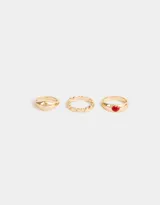 Set de tres anillos dorados de metal con diferentes diseños: uno liso, uno con corazones y uno con un corazón rojo.