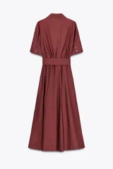 Vestido midi camisero color ladrillo, confeccionado en popelina de algodón. Presenta cuello solapa, manga corta con puños abotonados, bolsillos laterales ocultos y bolsillos de parche con solapa en el pecho. Incluye cinturón lazada en el mismo tejido y cierre frontal con botones ocultos.