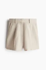 Short color beige de tiro alto con pliegues delanteros, bolsillos al bies y cierre frontal con botón y corchete ocultos.