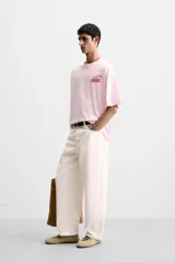 Camiseta rosa de corte holgado, cuello redondo y manga corta. Estampado frontal con texto en rojo "Amalfi Coast" y estrellas.