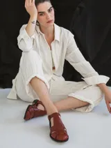 Sandalia roja de cuero vacuno con diseño de tiras entrecruzadas y hebilla lateral. Tiene suela de cuero artesanal y taco bajo.