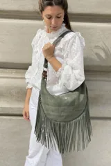 Bandolera de cuero color beige con flecos largos en la parte inferior y aplique de flor de lis en el frente. Tiene correa larga regulable y bolsillo con cierre en la parte trasera.