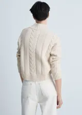 Sweater color crema de tejido de punto grueso con trenzas, cuello alto y mangas largas.