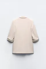 Blazer blanco con cuello solapa y hombreras. Manga por debajo del codo acabada en vuelta con trabilla y botón dorado. Bolsillos delanteros con solapa.