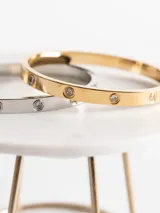 Brazalete de acero quirúrgico con circonitas, disponible en acabados de oro, oro rosa o plata.