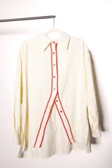 Camisa de popelina de algodón a rayas blancas y amarillas, de corte holgado, con cuello clásico, mangas largas y abertura frontal con botones rojos y ribete festoneado rojo.